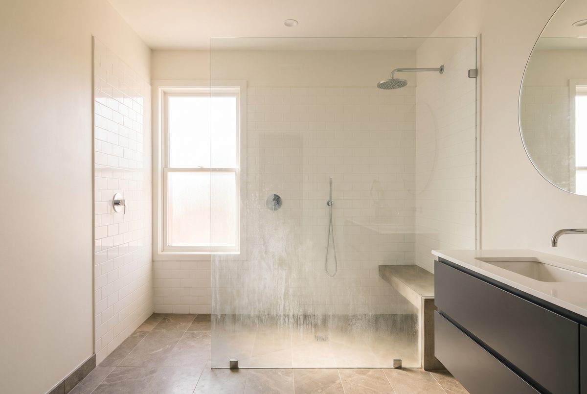 A tiled walk-in shower with a glass panel showing cloudy white mineral scale across the lower half of the glass.