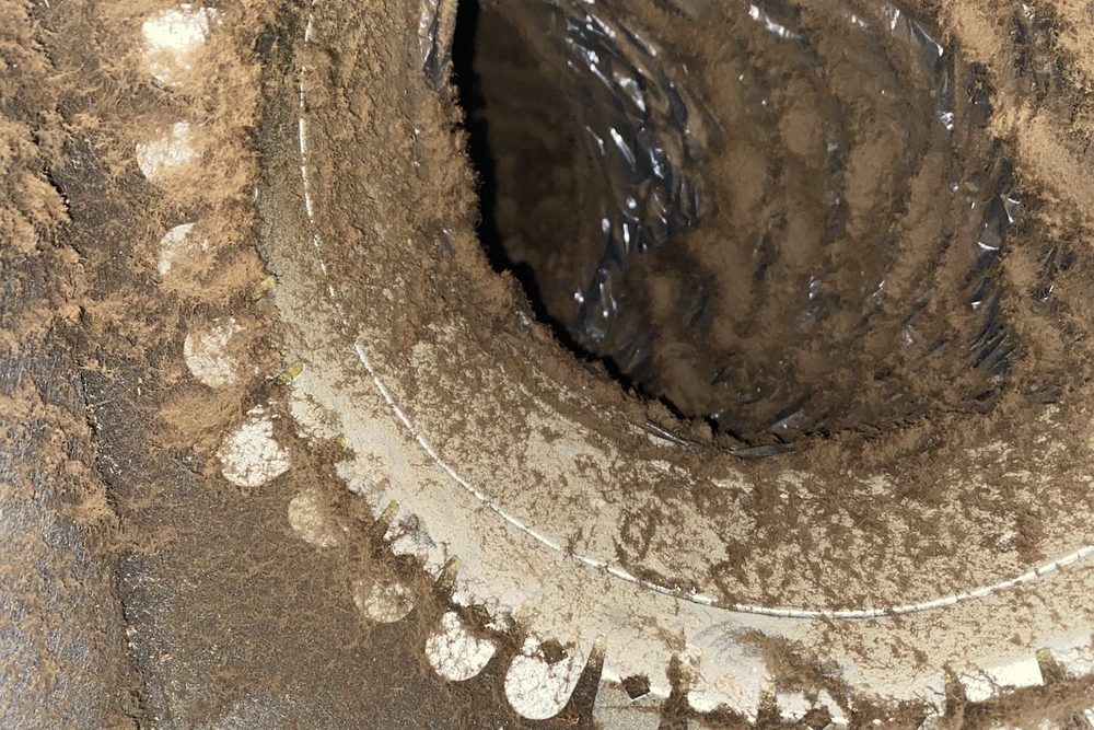 Close-up of a duct collar coated in thick brown dust