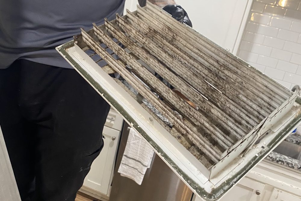 A technician holding a return air grille with dust packed between the slats