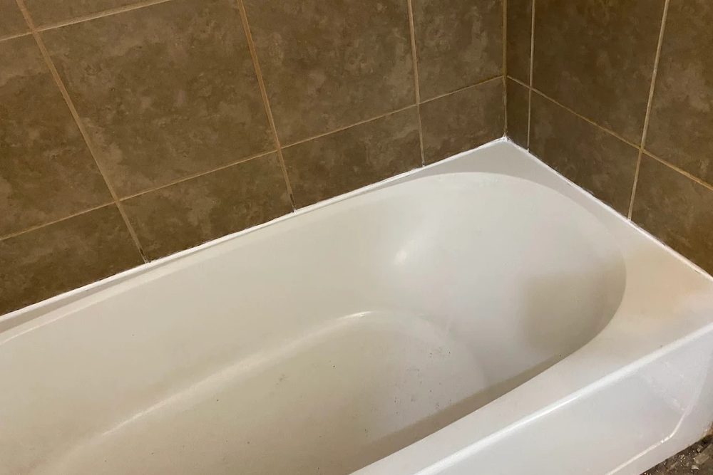A white bathtub set into a brown ceramic tile surround